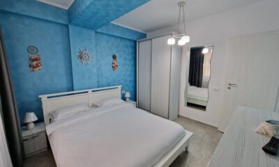Un dormitor frumos amenajat cu pereți albaștri, un pat alb și decorațiuni cu tematică nautică în cazare apartamente Mamaia Nord.